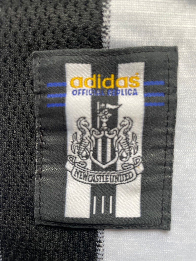 May include: Black and white adidas football shirt patch with the Newcastle United crest and the text "adidas Official Replica".