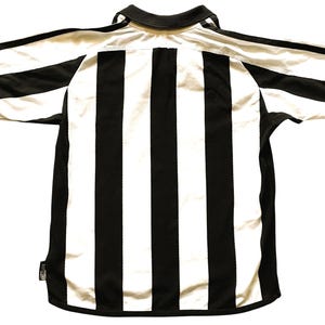 May include: A black and white striped football shirt with short sleeves. The shirt has a black collar and black trim on the sleeves. The sleeve cuffs have a blue accent. The shirt is laid flat.