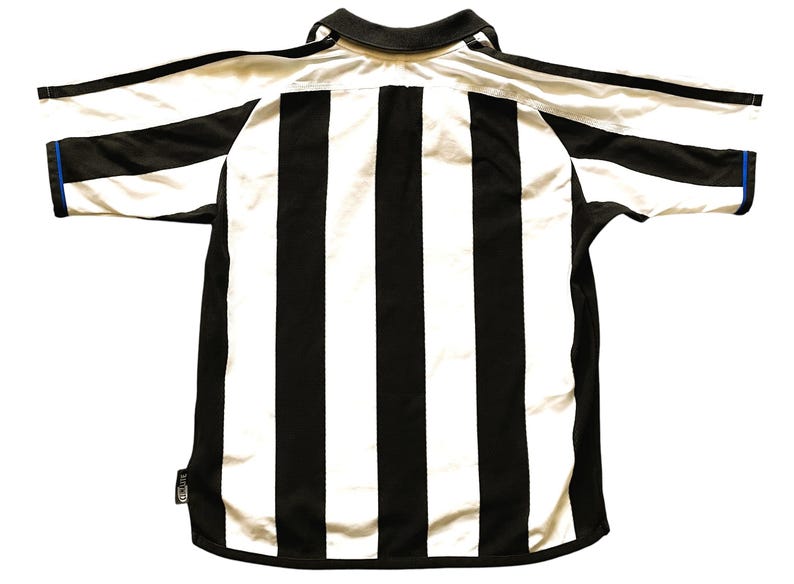 May include: A black and white striped football shirt with short sleeves. The shirt has a black collar and black trim on the sleeves. The sleeve cuffs have a blue accent. The shirt is laid flat.