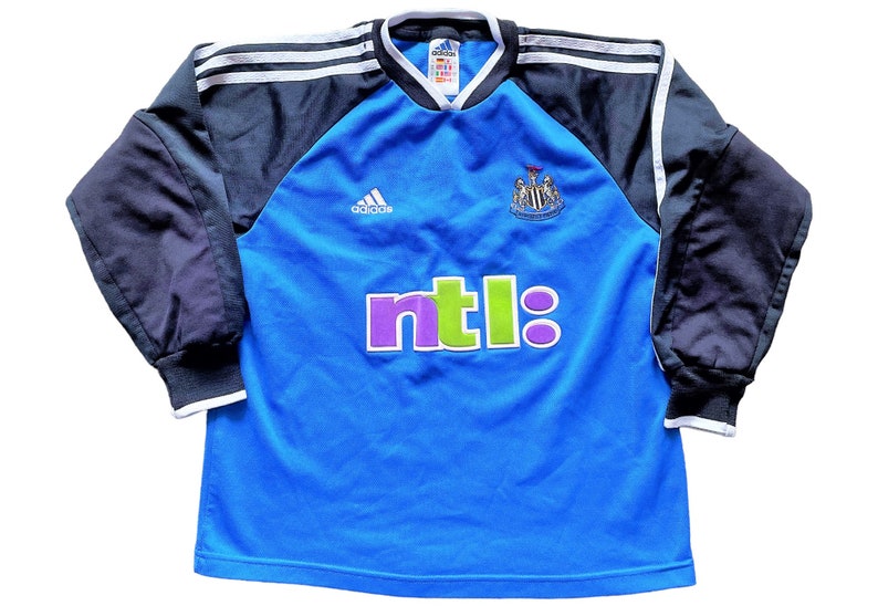 May include: A blue long-sleeved soccer jersey with black sleeves and white stripes. The jersey has the Adidas logo, the Newcastle United crest, and the NTL logo.