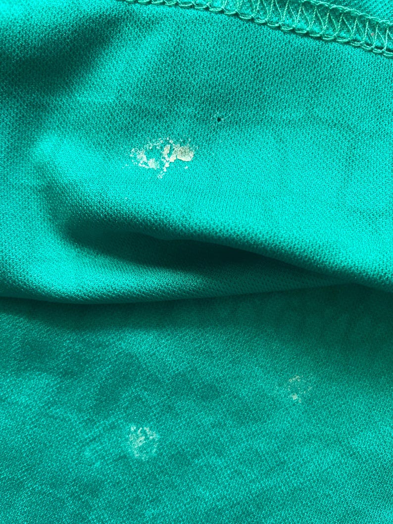 May include: Close-up of a teal fabric with visible texture and stitching. The fabric has several small, light-colored spots. The image highlights the material's weave and the color's saturation.