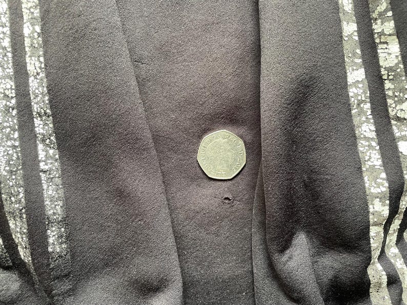 May include: Black fabric with silver stripes. The fabric has a small hole in the centre.