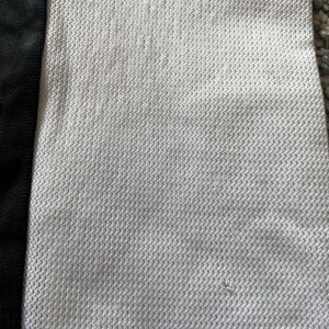 May include: Close-up of a white fabric with a textured, woven pattern. The fabric has a black stripe running down the left side.