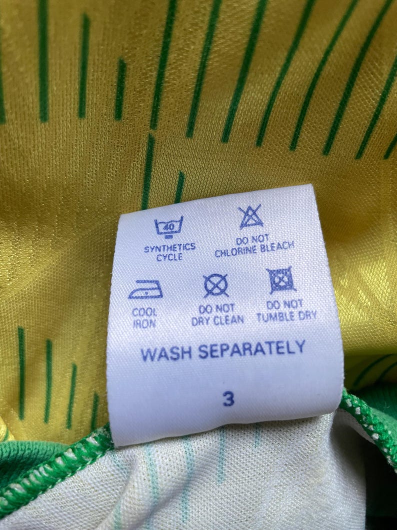 May include: White care label with blue text and symbols. The label includes instructions for washing, drying, and ironing a garment. The text reads "Synthetics Cycle", "Do Not Chlorine Bleach", "Cool Iron", "Do Not Dry Clean", "Do Not Tumble Dry", and "Wash Separately". The number "3" is printed at the bottom of the label.