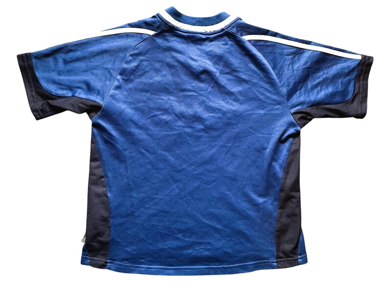 Op de afbeelding: Een blauw sportshirt met zwarte zijpanelen en mouwen. Witte strepen lopen langs de schouders. De kraag is wit met een blauwe bies. Het shirt is gemaakt van lichtgewicht, ademend materiaal.