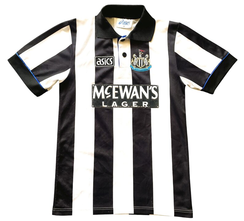 May include: A black and white striped soccer jersey with a black collar and sleeves. The jersey features the "Asics" logo, a team crest, and the "McEwan's Lager" logo. The sleeves have blue trim.