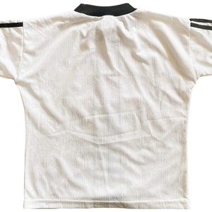 May include: White short-sleeved t-shirt with black trim around the collar and black stripes on the sleeves.