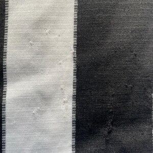 May include: Close-up of a fabric with vertical black and white stripes. The fabric has a blue border at the bottom. The fabric appears to be knit or woven, with some minor imperfections visible.