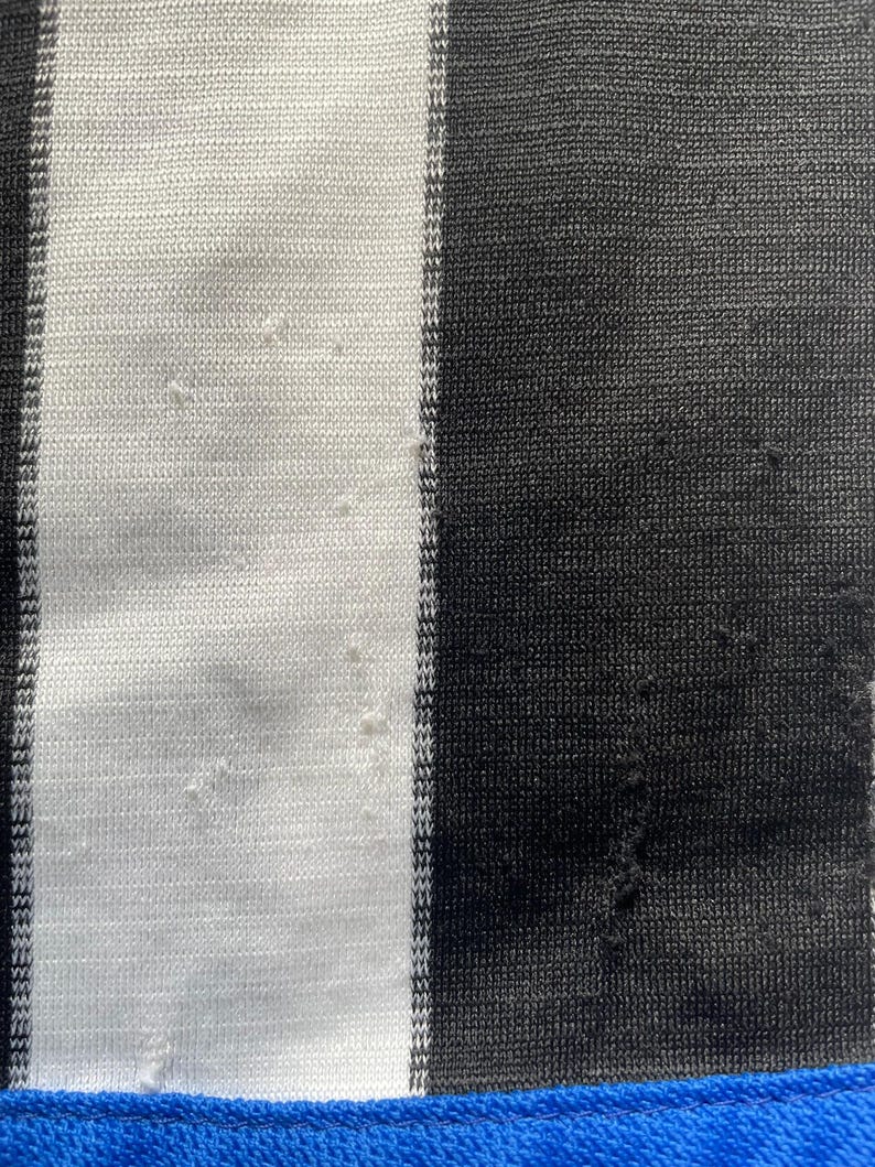 May include: Close-up of a fabric with vertical black and white stripes. The fabric has a blue border at the bottom. The fabric appears to be knit or woven, with some minor imperfections visible.