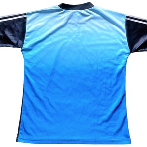 K&ouml;nnte beinhalten: Ein blaues und schwarzes Fu&szlig;balltrikot mit wei&szlig;en Akzenten. Das Trikot hat ein Farbverlaufsdesign, das von Hellblau zu Dunkelblau &uuml;bergeht.