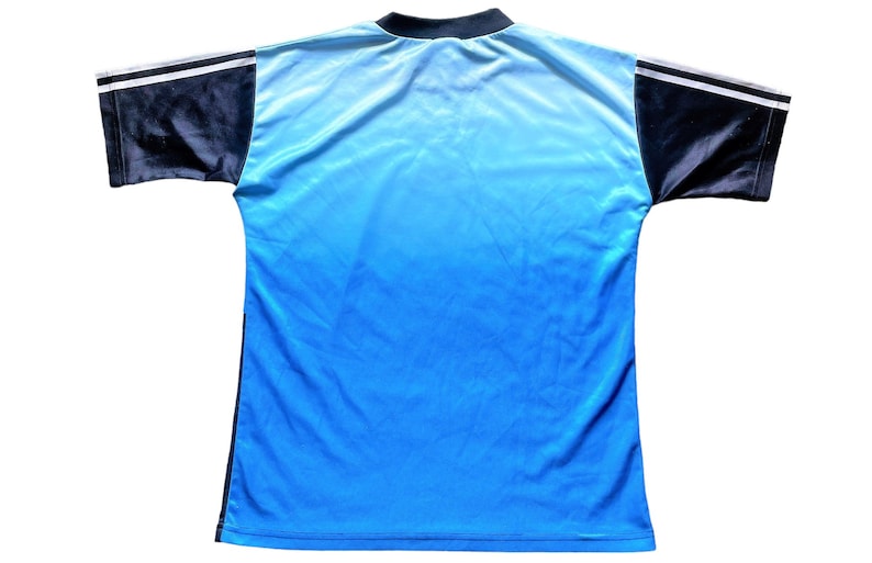 K&ouml;nnte beinhalten: Ein blaues und schwarzes Fu&szlig;balltrikot mit wei&szlig;en Akzenten. Das Trikot hat ein Farbverlaufsdesign, das von Hellblau zu Dunkelblau &uuml;bergeht.