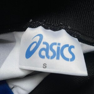 May include: Close-up of a white tag with the blue "asics" logo and the letter "S". The tag is attached to a black and white patterned fabric. The tag is slightly wrinkled.