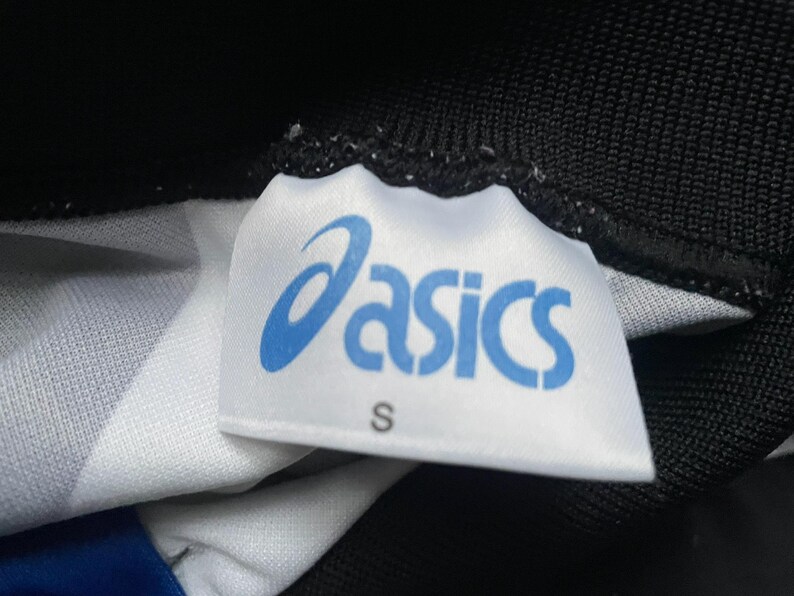 May include: Close-up of a white tag with the blue "asics" logo and the letter "S". The tag is attached to a black and white patterned fabric. The tag is slightly wrinkled.