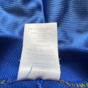 K&ouml;nnte beinhalten: Ein wei&szlig;es Etikett mit schwarzem Text auf blauem Hintergrund. Das Etikett lautet "Die Weltmarke mit den Streifen", "The Brand with the Stripes", "La Marque aux Bandes", "100% Polyester", "Waschen und Seselinordka", "Wash and Iron Inside Out", "Lavage et Repassage a l'envers", "Made in UK", "Fabrique au Royaume Uni".