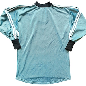 K&ouml;nnte beinhalten: Ein tealfarbenes Langarmshirt mit wei&szlig;en Streifen auf den &Auml;rmeln und einem schwarzen Kragen und B&uuml;ndchen. Das Shirt hat ein sportliches Design und eine gerippte Textur.