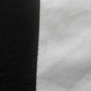 Puede incluir: Primer plano de una tela con una franja negra vertical a la izquierda y una franja blanca a la derecha. La tela tiene un aspecto texturizado, con l&iacute;neas horizontales visibles. El contraste entre el blanco y el negro crea un efecto visual audaz.
