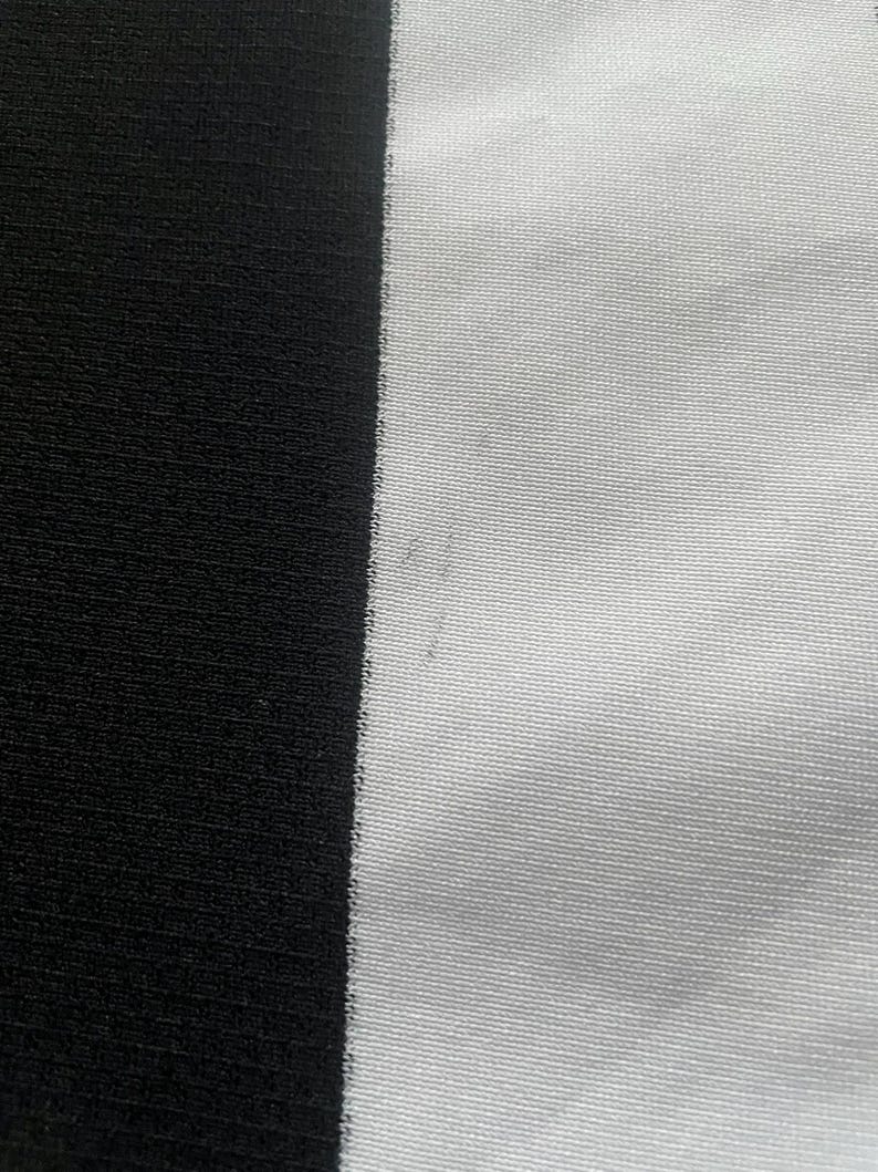 Puede incluir: Primer plano de una tela con una franja negra vertical a la izquierda y una franja blanca a la derecha. La tela tiene un aspecto texturizado, con l&iacute;neas horizontales visibles. El contraste entre el blanco y el negro crea un efecto visual audaz.