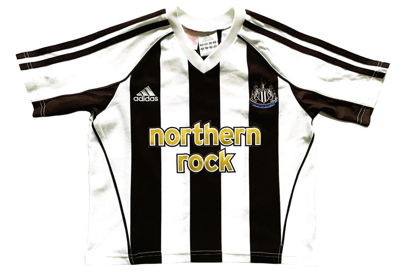 May include: White and black striped soccer jersey with brown accents and the text "northern rock". Features the Adidas logo and a team crest. The jersey has a V-neck collar.