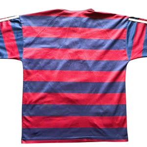 May include: A red and navy blue striped t-shirt with short sleeves. The shirt has horizontal stripes and white accents on the sleeves. The shirt is made of a shiny material.