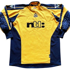 May include: Yellow and blue long-sleeved soccer jersey with the Newcastle United crest and the NTL logo.
