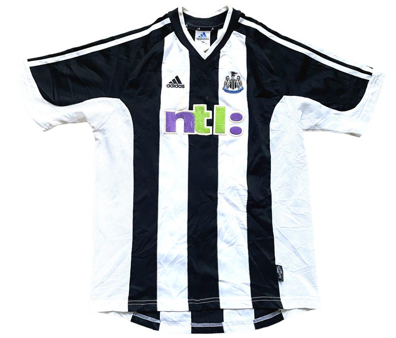 May include: Black and white striped soccer jersey with the Adidas logo, a Newcastle United crest, and the word "ntl:" in green and purple letters.