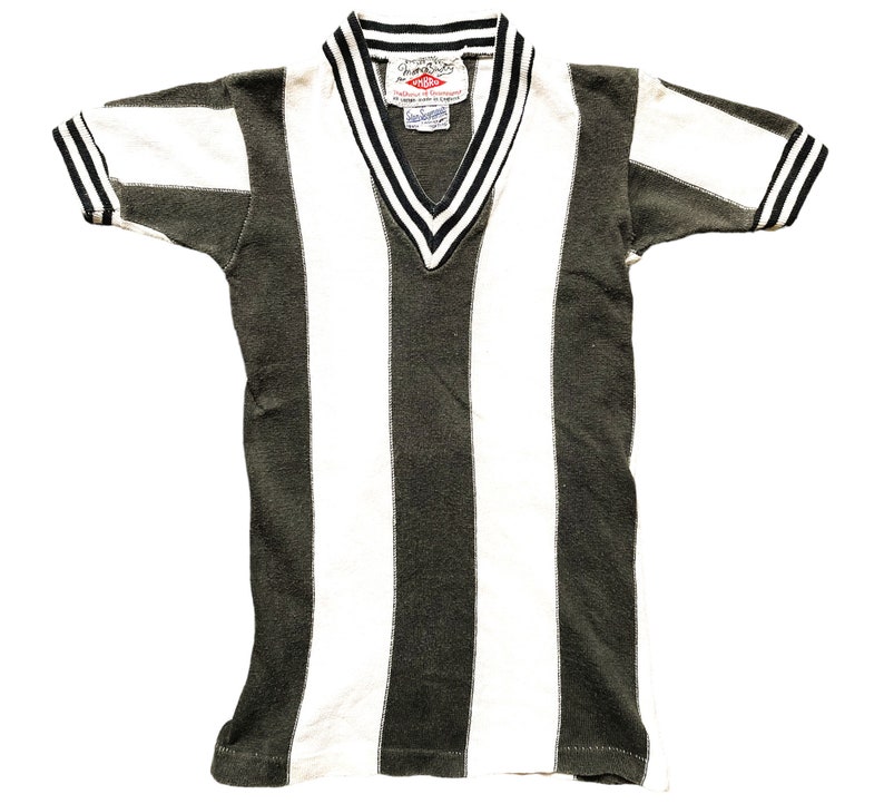 Puede incluir: Una camiseta vintage a rayas con cuello en V y mangas cortas. La camiseta es negra y blanca con una raya verde oscura en el centro. La camiseta tiene una peque&ntilde;a etiqueta con el texto "Champion" y "Made in USA" en la parte delantera.