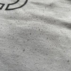 May include: Close-up of a grey fabric with a subtle texture. The fabric has small black specks throughout.