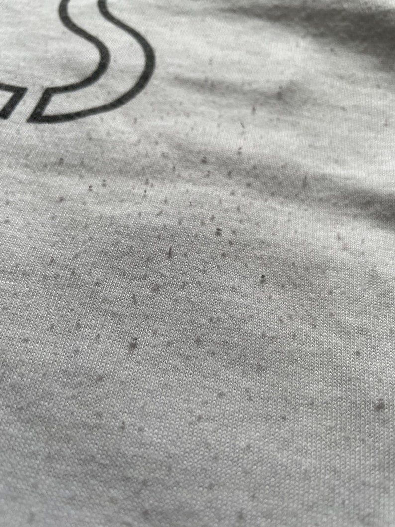 May include: Close-up of a grey fabric with a subtle texture. The fabric has small black specks throughout.