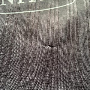 May include: Close-up of black fabric with a vertical ribbed texture. The word "UNITED" is visible in white block letters at the top. The fabric has a small tear.