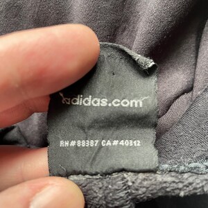 May include: Black clothing tag with white text that reads "adidas.com", "RN # 88387 CA # 40312".