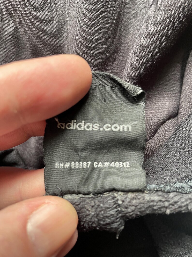 May include: Black clothing tag with white text that reads "adidas.com", "RN # 88387 CA # 40312".