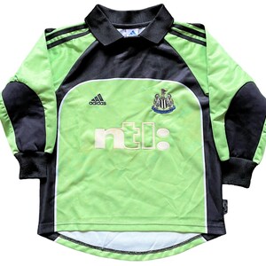May include: Green and black soccer jersey with long sleeves. The jersey has the Adidas logo, the Newcastle United crest, and the NTL logo.