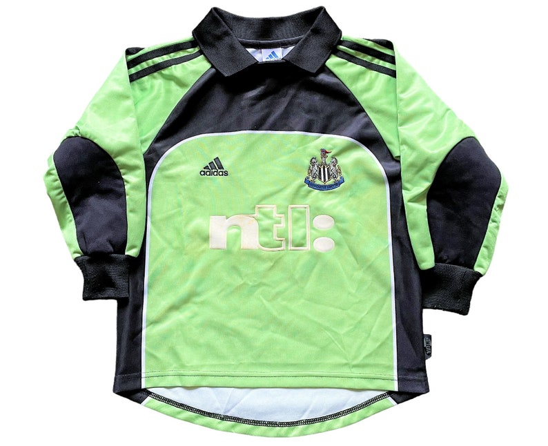 May include: Green and black soccer jersey with long sleeves. The jersey has the Adidas logo, the Newcastle United crest, and the NTL logo.
