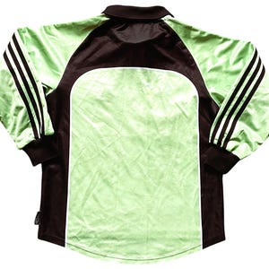 May include: A long-sleeved soccer jersey with black and white stripes on the sleeves. The jersey is green and has a black collar and black accents on the sides.