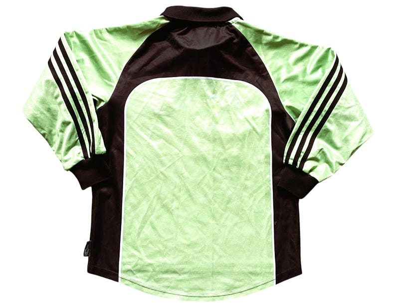 May include: A long-sleeved soccer jersey with black and white stripes on the sleeves. The jersey is green and has a black collar and black accents on the sides.