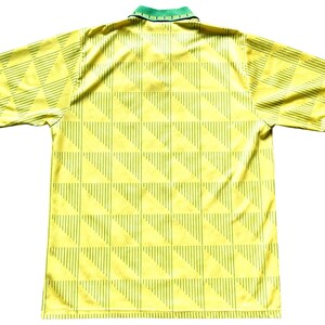 May include: A yellow and green soccer jersey with a geometric pattern. The jersey has a collar and short sleeves.