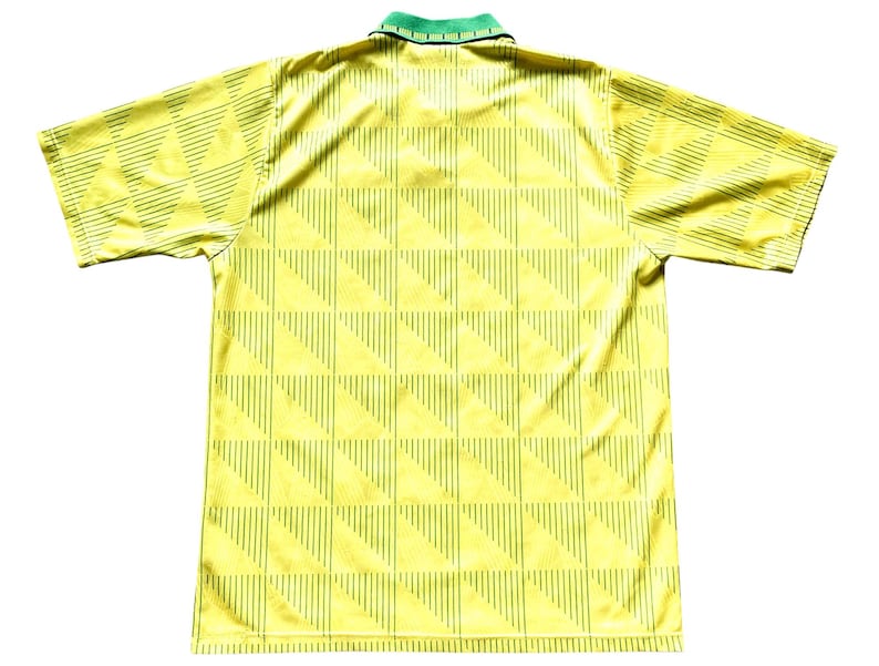 May include: A yellow and green soccer jersey with a geometric pattern. The jersey has a collar and short sleeves.