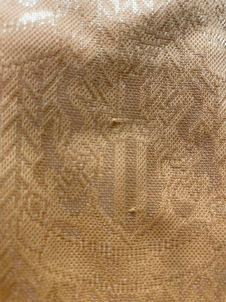 May include: Close-up of a textured fabric in a warm, golden-brown hue. The material features a repeating pattern of small, raised squares and subtle geometric designs, creating a tactile and visually interesting surface. The fabric appears to be woven.