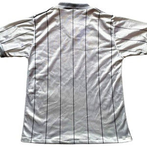 May include: White striped soccer jersey with a black collar and black trim on the sleeves.