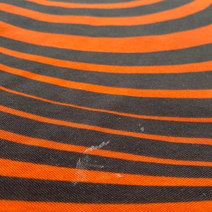 May include: A close-up of a black and orange striped fabric with a swirling pattern. The fabric has a textured surface.
