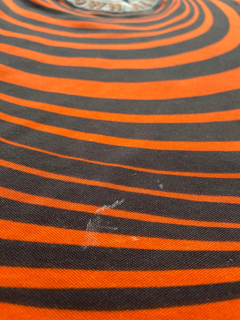 May include: A close-up of a black and orange striped fabric with a swirling pattern. The fabric has a textured surface.