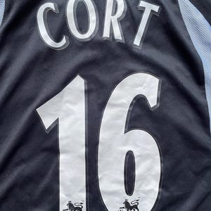 May include: Black soccer jersey with white lettering that reads "Cort 16". The jersey has the logo of the FA Premier League on the bottom.
