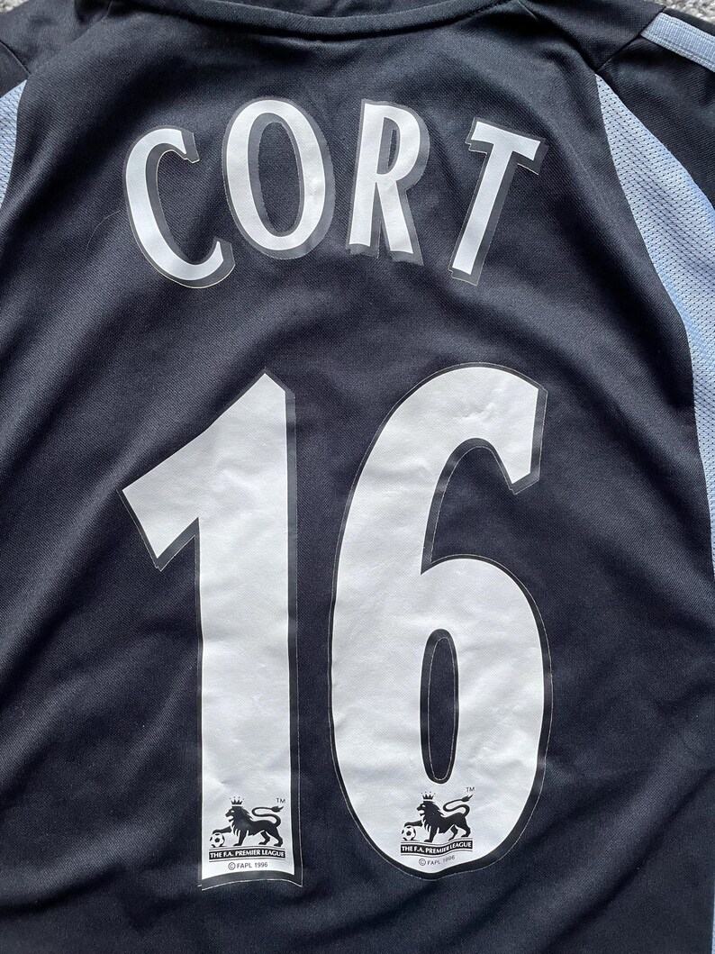 May include: Black soccer jersey with white lettering that reads "Cort 16". The jersey has the logo of the FA Premier League on the bottom.