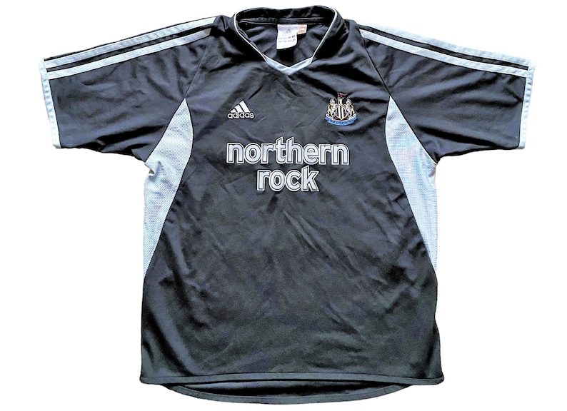 May include: A black football shirt with white accents. The shirt features the Adidas logo, the Newcastle United crest, and the text "northern rock" on the front.