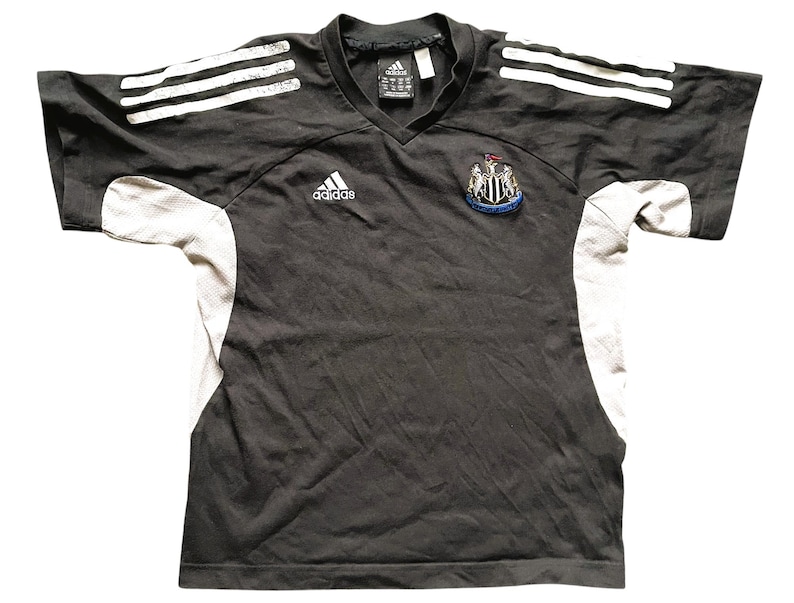 May include: Black and white soccer jersey with the Adidas logo and the Newcastle United Football Club crest. The jersey has white stripes on the shoulders and sleeves.