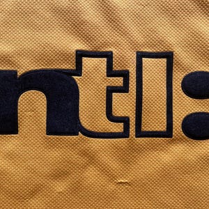 May include: A yellow fabric patch with the text "ntl:" in black.