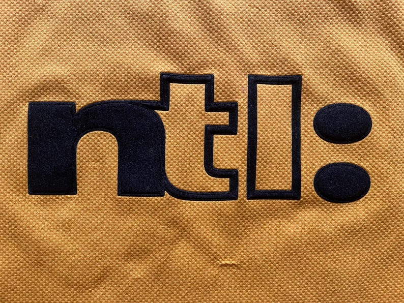 May include: A yellow fabric patch with the text "ntl:" in black.