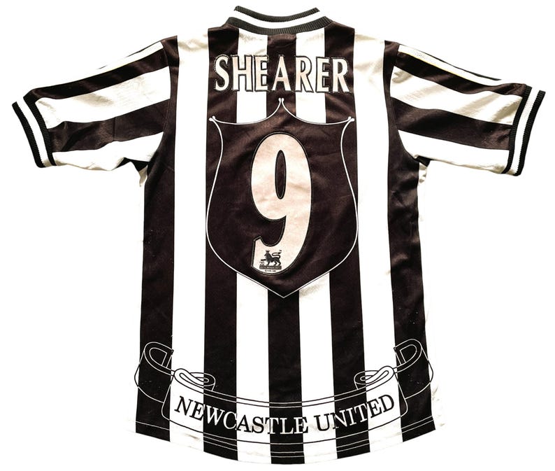 May include: A black and white striped Newcastle United soccer jersey. The jersey features the name "SHEARER" and the number "9" on the back. The team name "NEWCASTLE UNITED" is displayed on a banner at the bottom.