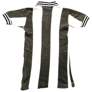 Puede incluir: Una camiseta polo de rayas blancas y negras con cuello negro y ribetes negros en las mangas.