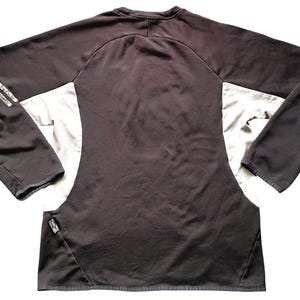 May include: Black and white long-sleeved athletic shirt with a silver stripe detail on the sleeves. The shirt has a crew neck and a fitted silhouette.